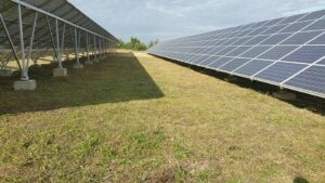 Installation d'une ferme photovoltaïque. Panneaux solaires fixés sur structure métallique et fondations en béton, chemin herbeux.